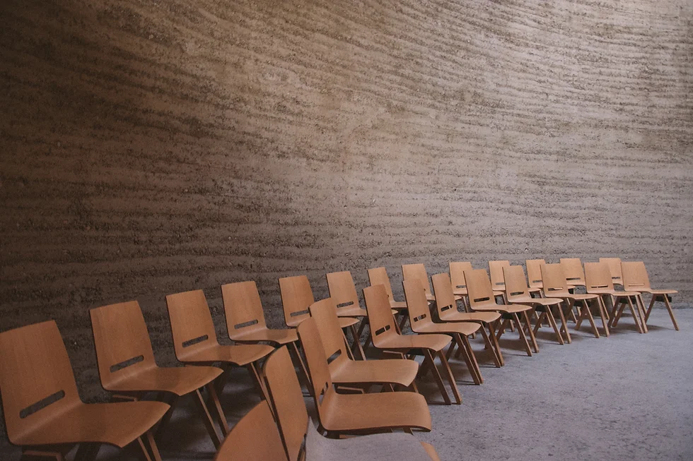 Rows of empty wooden chairs against a textured beige concrete wall, warm earthy tones, calm minimalist mood